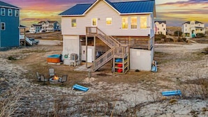 Ein zweistöckiges Strandhaus mit einer Holzterrasse und einer Treppe, die zu einem Balkon führt.