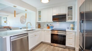 A modern kitchen with white cabinetry, stainless steel appliances, and a central island with a dishwasher. - Completely Remodeled Direct Ocean View Colony Reef Condo 3401 (St Augustine)