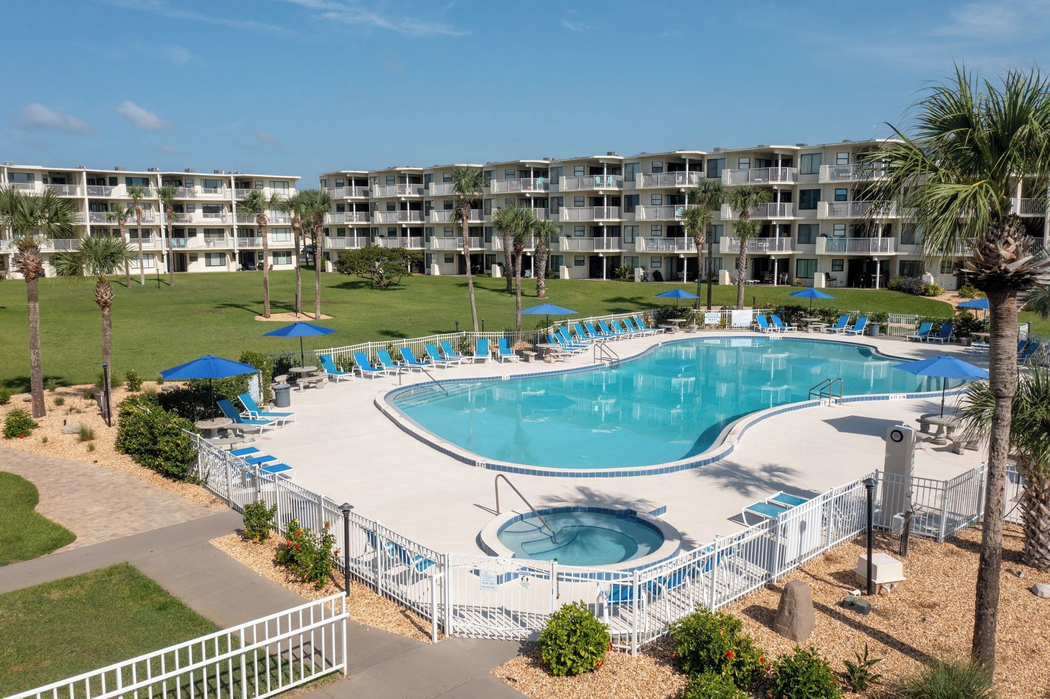 A hotel pool area with a large pool, sun loungers, and a hot tub.