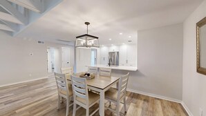 Une cuisine moderne avec des meubles blancs, un réfrigérateur en acier inoxydable et un coin repas comprenant une table en bois et des chaises blanches.