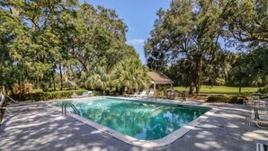 Une piscine avec des chaises longues et un kiosque entouré d’arbres.
