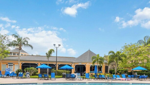 A pool area with lounge chairs and umbrellas, surrounded by palm trees and a building with a grey roof. - Bahama Bay- 3 bedroom condo with amenities (Davenport)