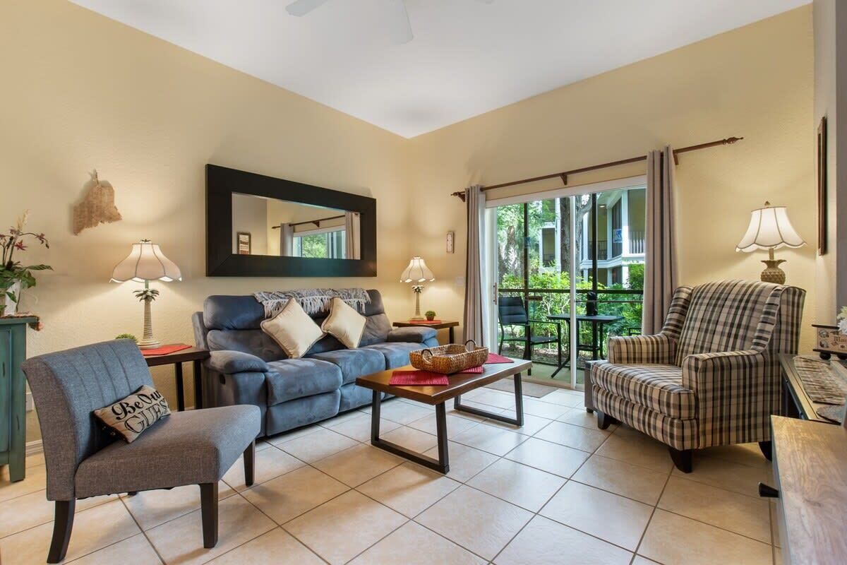 A living room with a sofa, armchair, and a table with a lamp.
