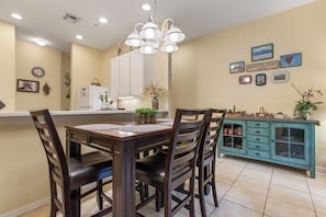 A dining area with a wooden table and chairs, a white refrigerator, a teal cabinet, and wall-mounted decorations.