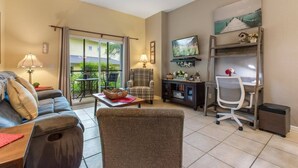 A living room with a sofa, armchair, coffee table, TV, desk, and computer. There is a sliding glass door leading to a balcony. - Bahama Bay- 3 bedroom condo with amenities (Davenport)