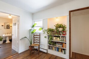 Une pièce d’angle avec un plancher en bois, une chaise, une bibliothèque et une fenêtre.