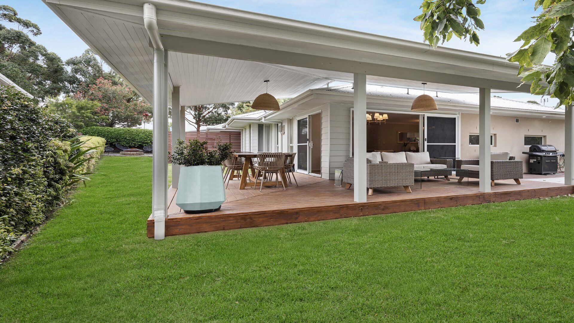 Un patio couvert aménagé avec du mobilier d’extérieur, un barbecue et une grande plante en pot.