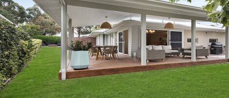 Un patio couvert aménagé avec du mobilier d’extérieur, un barbecue et une grande plante en pot.