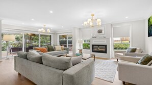 Un salón espacioso con un sofá seccional gris, una chimenea y un gran ventanal con vistas a un jardín.