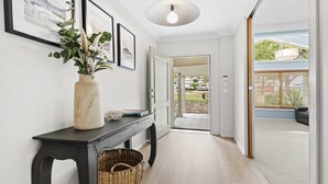 Un pasillo con una consola de madera oscura, un florero con flores, cuadros en la pared y vista a un patio trasero a través de una puerta abierta.