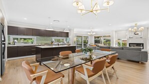 Una cocina moderna con armarios oscuros, una isla central y un comedor con mesa de vidrio y sillas marrones.