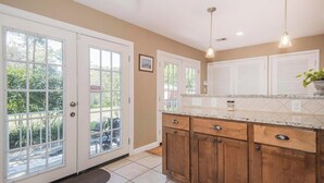 A kitchen with wooden cabinets, a marble countertop, and a view through the glass doors. - Come to Pensacola White Sand beaches, in a great location 🏚️ (Pensacola)