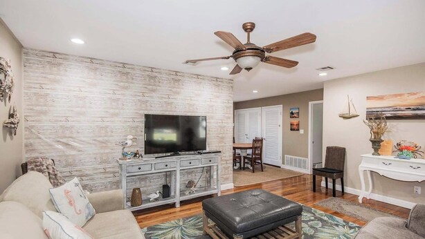 A living room with a TV, wooden furniture, a ceiling fan, and a dining area. - Come to Pensacola White Sand beaches, in a great location 🏚️ (Pensacola)