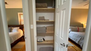 A bedroom with a wooden floor, a bed with white bedding, and a closet with shelves and a pet bed. - Come to Pensacola White Sand beaches, in a great location 🏚️ (Pensacola)