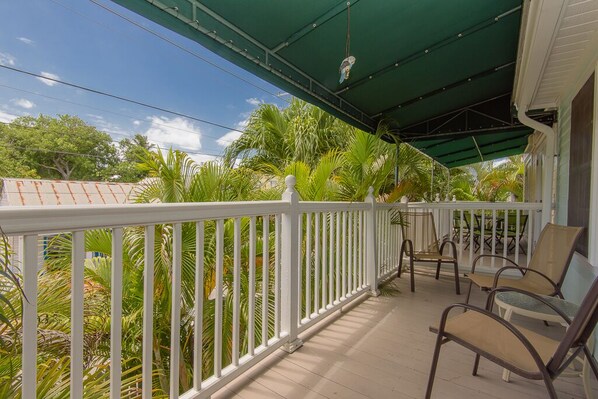 A covered porch with white railings, outdoor furniture, and lush greenery. - Tropical Breezes at The Truman Annex in Key West (Key West)