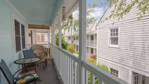 A covered porch with a table and chairs, white railings, and a view of neighboring houses. - Tropical Breezes at The Truman Annex in Key West (Key West)