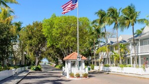 A street view with a flagpole, a small gazebo, and a row of white buildings with balconies. - Tropical Breezes at The Truman Annex in Key West (Key West)