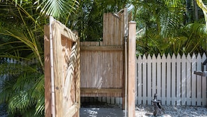 A wooden gate leading to a covered outdoor area with a white picket fence and a stone fountain.