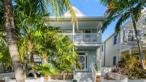 A two-story house with a white picket fence, palm trees, and a clear blue sky.