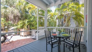 A covered patio with a table and chairs, surrounded by a white fence and lush tropical plants.