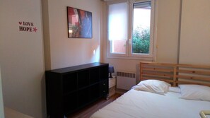 A bedroom with a bed, a black TV stand, a window, and a wall decoration. - Résidence le Pastel François Verdier (Toulouse)