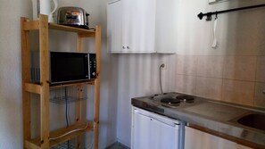 A compact kitchen with a microwave on a wooden shelf, a small refrigerator, and a gas stove. - Résidence le Pastel François Verdier (Toulouse)