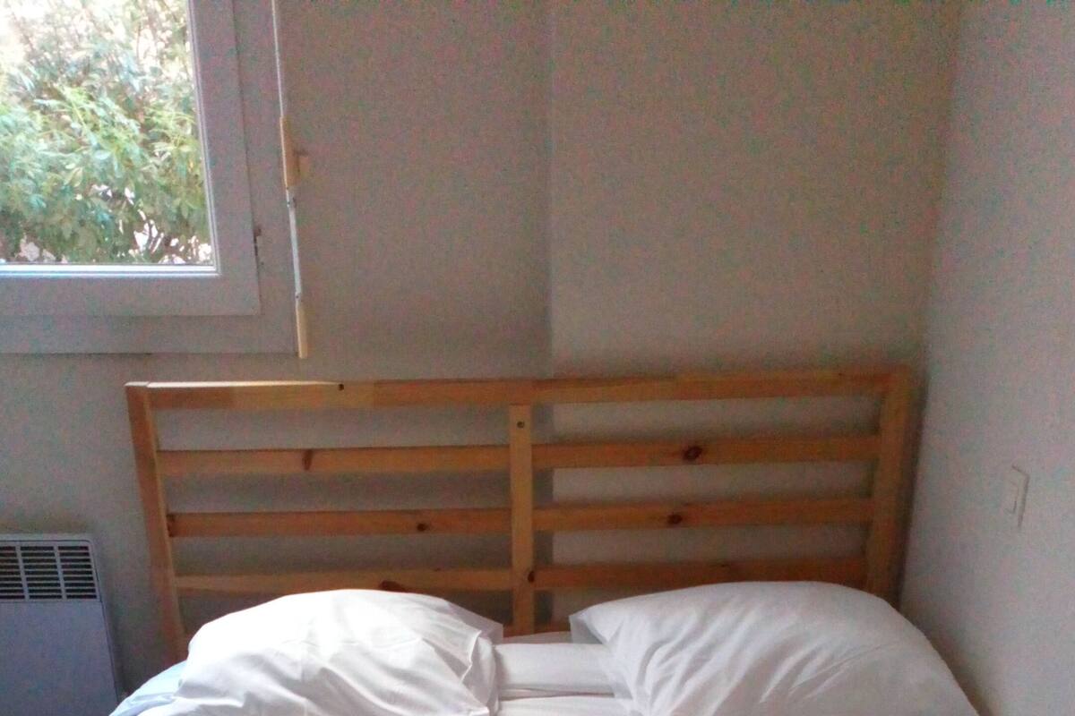 Un lit avec une tête de lit en bois, dans une pièce dotée d’une fenêtre et d’un radiateur.