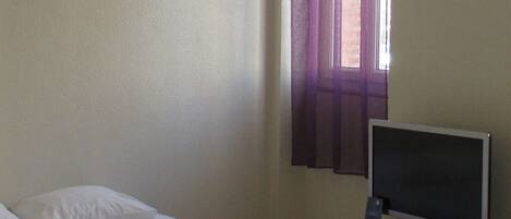 A simple room with a bed, a television on a stand, and a window with purple curtains.