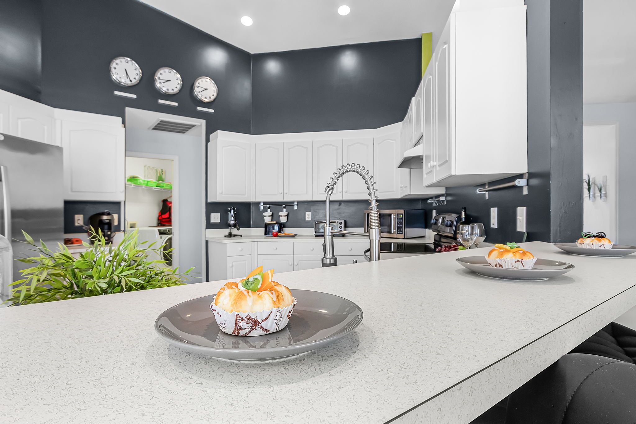A modern kitchen with white cabinets, a central island with baked goods, and a black accent wall.