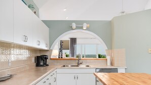 Una cocina moderna con armarios blancos, encimera de madera y vistas a través de un ventanal arqueado.