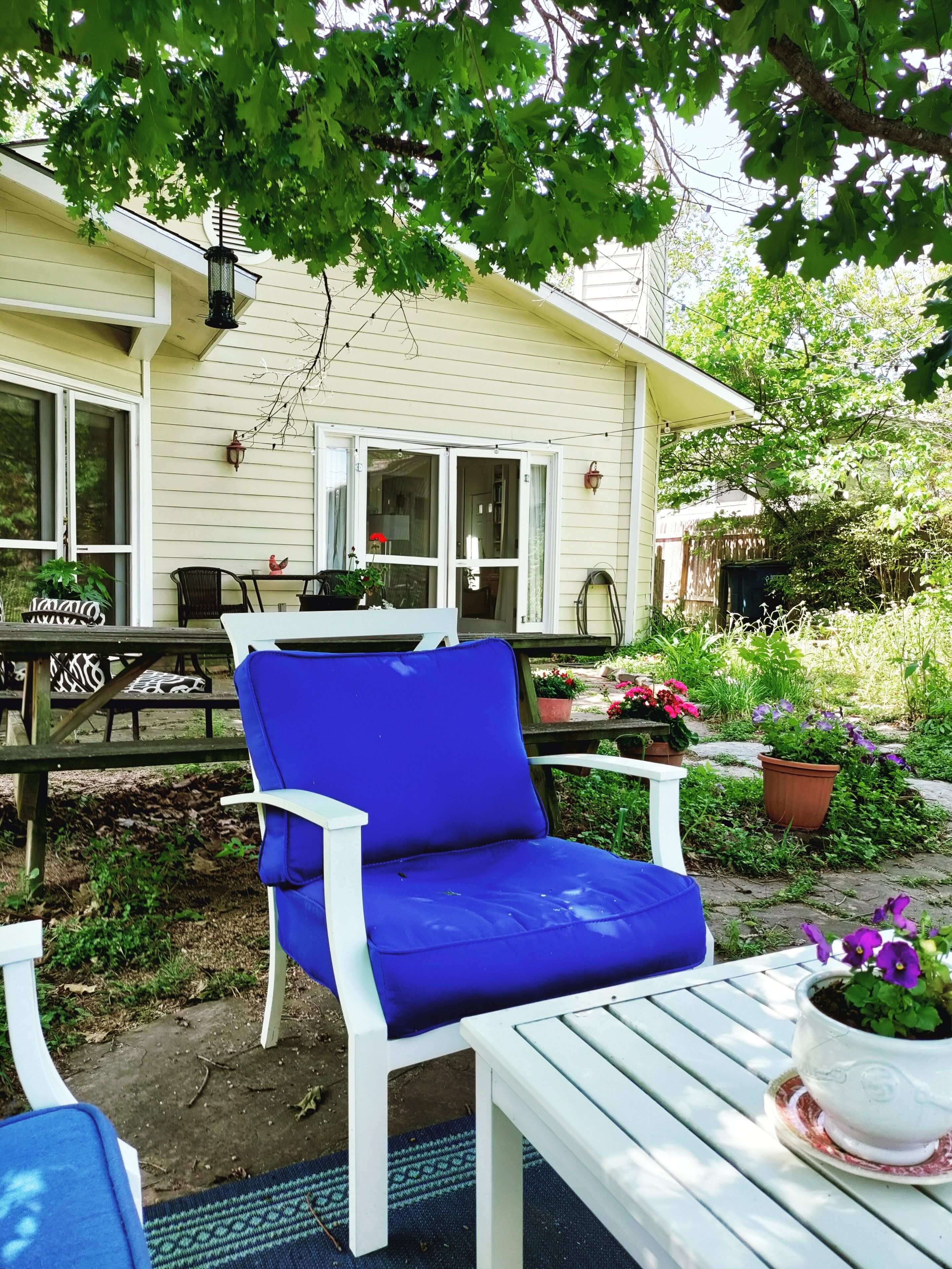 A patio with a blue chair, a white table, and a house in the background.