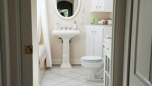 Une salle de bain comprenant un lavabo sur colonne, des toilettes, un miroir et un meuble de rangement.