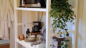 Un meuble blanc avec des étagères, sur lequel on trouve un four à micro-ondes, une machine à café et un pot de fleurs.