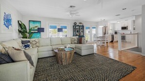 A spacious living room with a white sofa, a coffee table, and a large woven rug. There is a dining area with a table and chairs, and a kitchen in the background. - Marlin Blue at the Truman Annex in Key West (Key West)