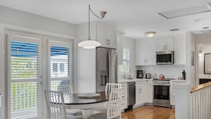 A modern kitchen with white cabinets, stainless steel appliances, and a dining area with white chairs. - Marlin Blue at the Truman Annex in Key West (Key West)