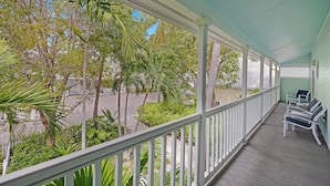 A covered porch with white railings, a row of chairs, and lush greenery in the background. - Marlin Blue at the Truman Annex in Key West (Key West)