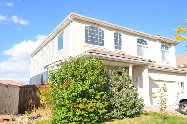 Traditional two-story home with a central entrance and front porch, set amidst a well-manicured lawn and shrubs.