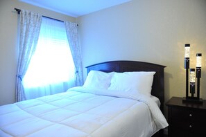 Cozy retreat with a neatly made bed, dark headboard, and bedside table with a lamp.