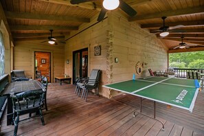 Una terraza de madera con mesa de ping pong, sillas y ventiladores de techo.