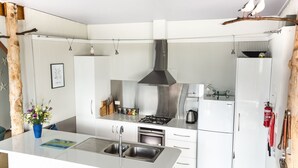 A modern kitchen with white cabinetry, a stainless steel range hood, a gas stove, an oven, and a sink. - Larus Waterfront Cottage (White Beach)