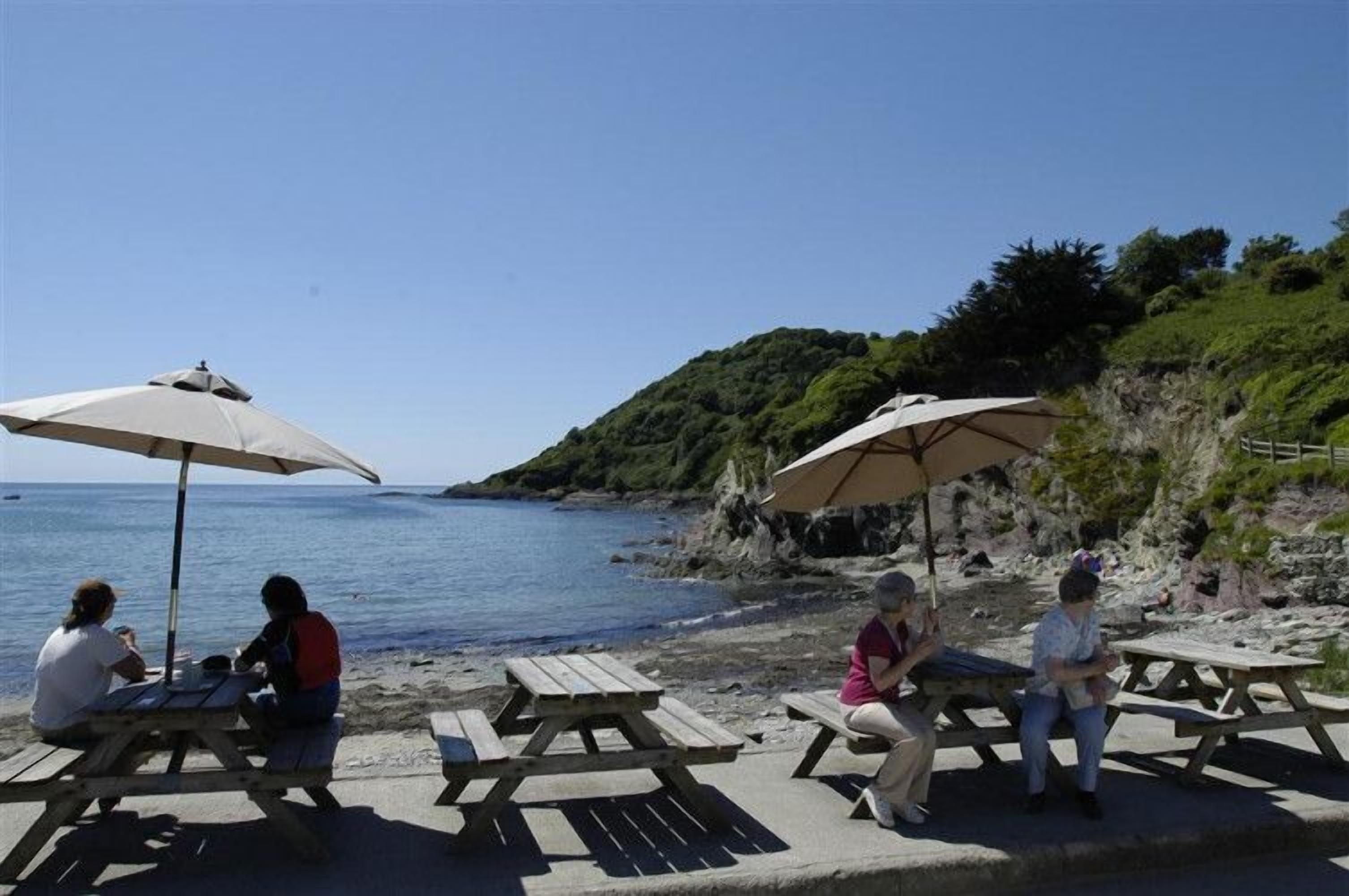 A beachside area with picnic tables and umbrellas, overlooking the sea.
