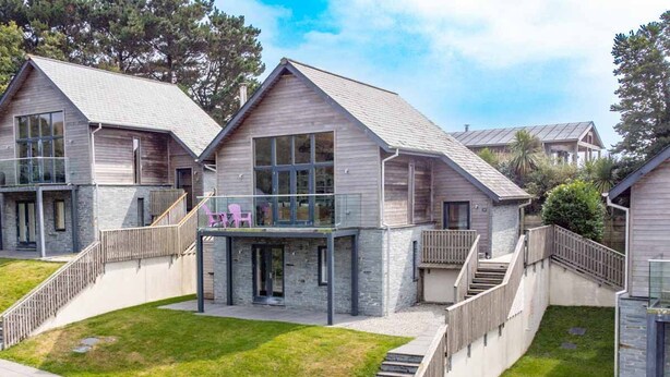 A modern multi-story house with a stone facade, large windows, and a balcony with outdoor seating. - Beautiful holiday home with hot tub, just a walk away from Talland beach... (Looe)