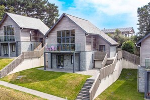 A modern multi-story house with a stone facade, large windows, and a balcony with outdoor seating. - Beautiful holiday home with hot tub, just a walk away from Talland beach... (Looe)
