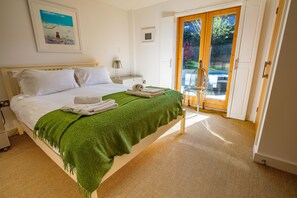 Ein ordentlich bezogenes Bett mit grüner Decke, einem weißen Kissen und einem zusammengerollten Handtuch. Ein kleiner Nachttisch mit Lampe und ein gerahmtes Bild an der Wand sind ebenfalls zu sehen.