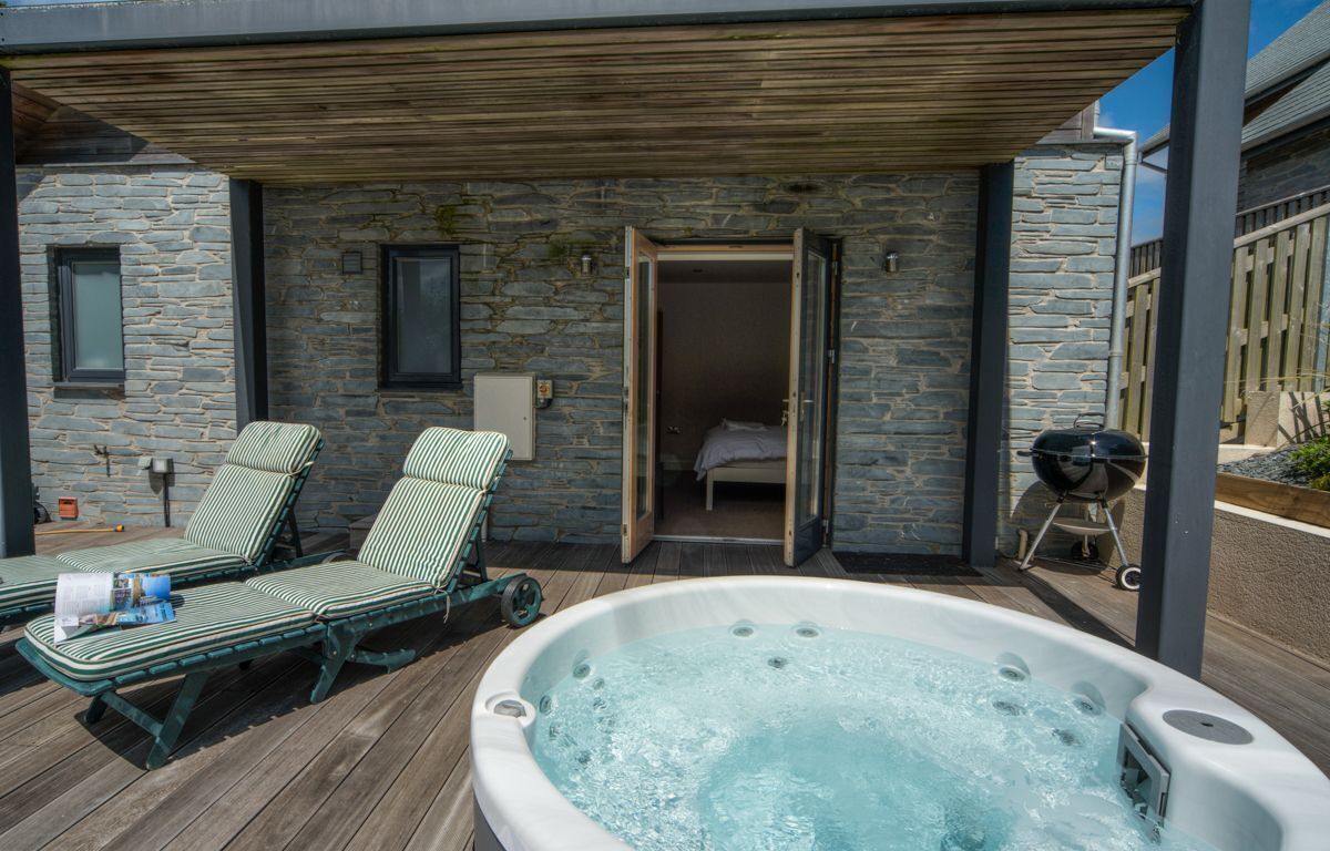 Un espace bien-être comprenant un bain à remous, deux chaises longues et un mur en pierre.