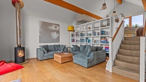 A cozy living room with a fireplace, grey sofas, a bookshelf, and a staircase. - Beautiful holiday home with hot tub, just a walk away from Talland beach... (Looe)