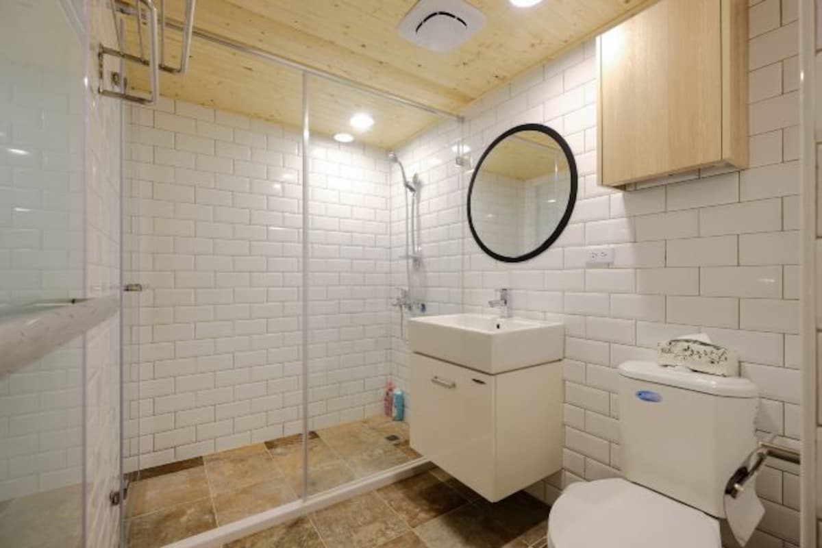 Un bany amb rajoles blanques de tipus metro, una cabina de dutxa de vidre, un lavabo blanc i un vàter.