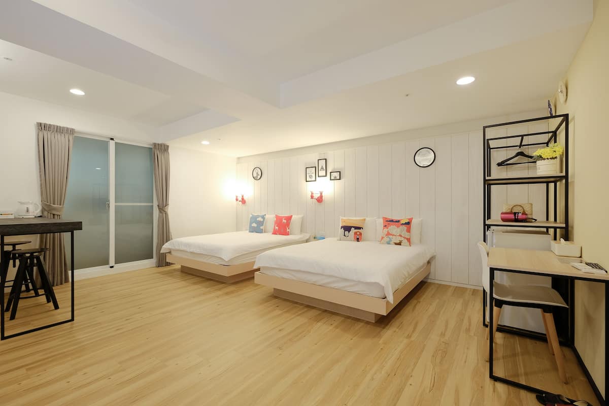 Quarto de hotel moderno com duas camas de solteiro, uma escrivaninha, uma cadeira e um pequeno espaço para sentar.