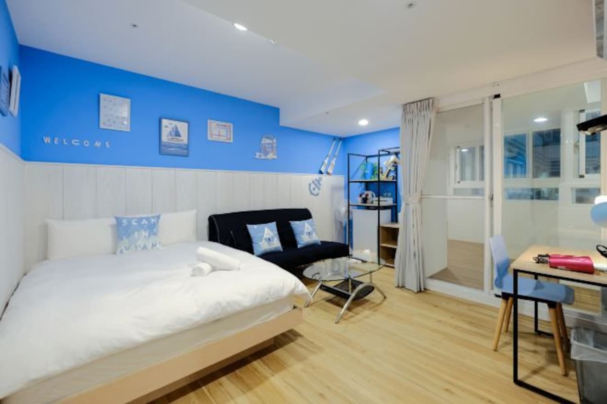 Habitació d'hotel moderna amb un llit, un sofà negre, una taula de vidre i un armari.