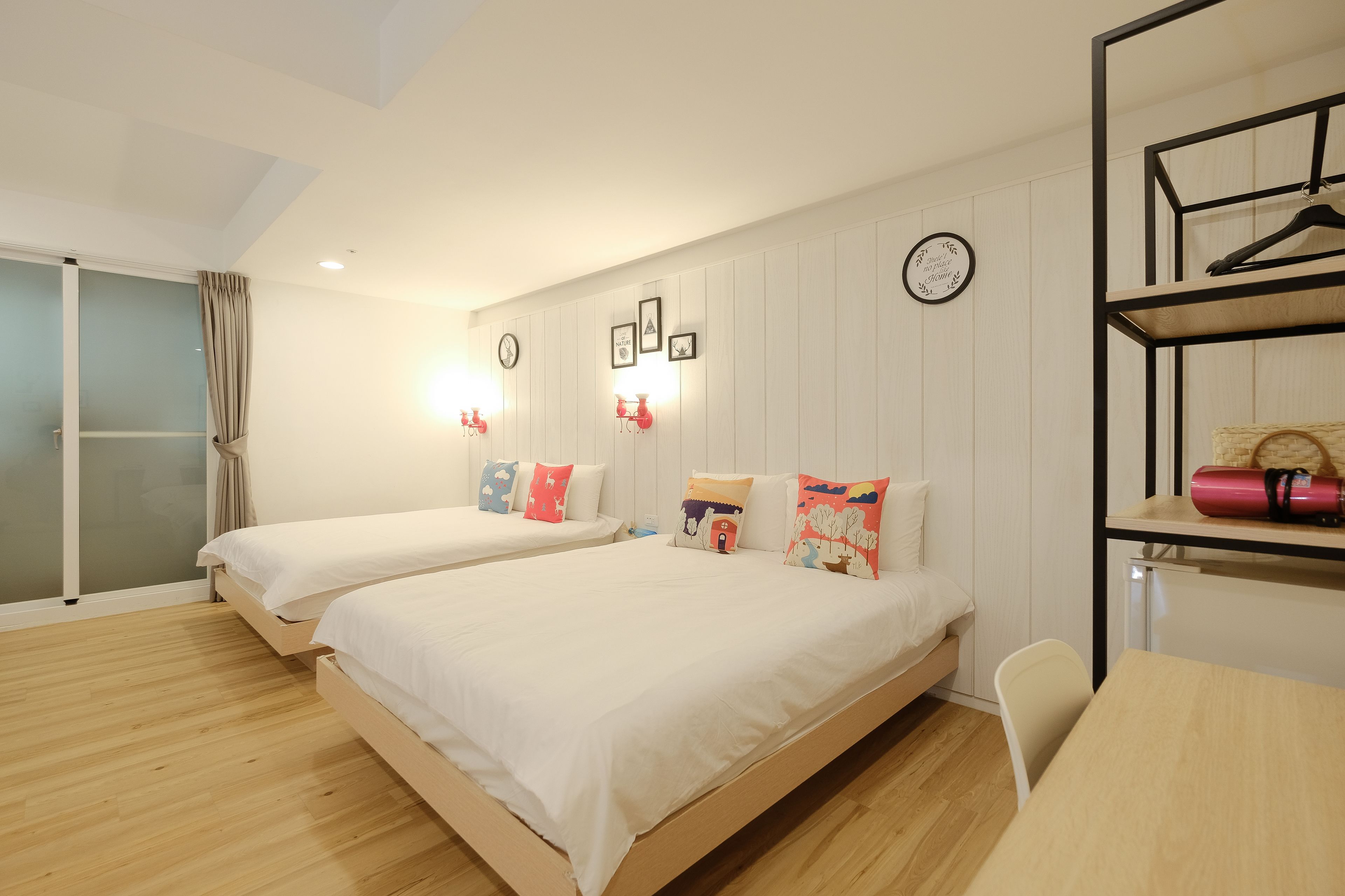 Quarto de hotel com duas camas, piso de madeira, escrivaninha e guarda-roupa com cabideiro.